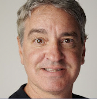 Man with short gray hair and a black shirt, smiling slightly at the camera against a plain background.